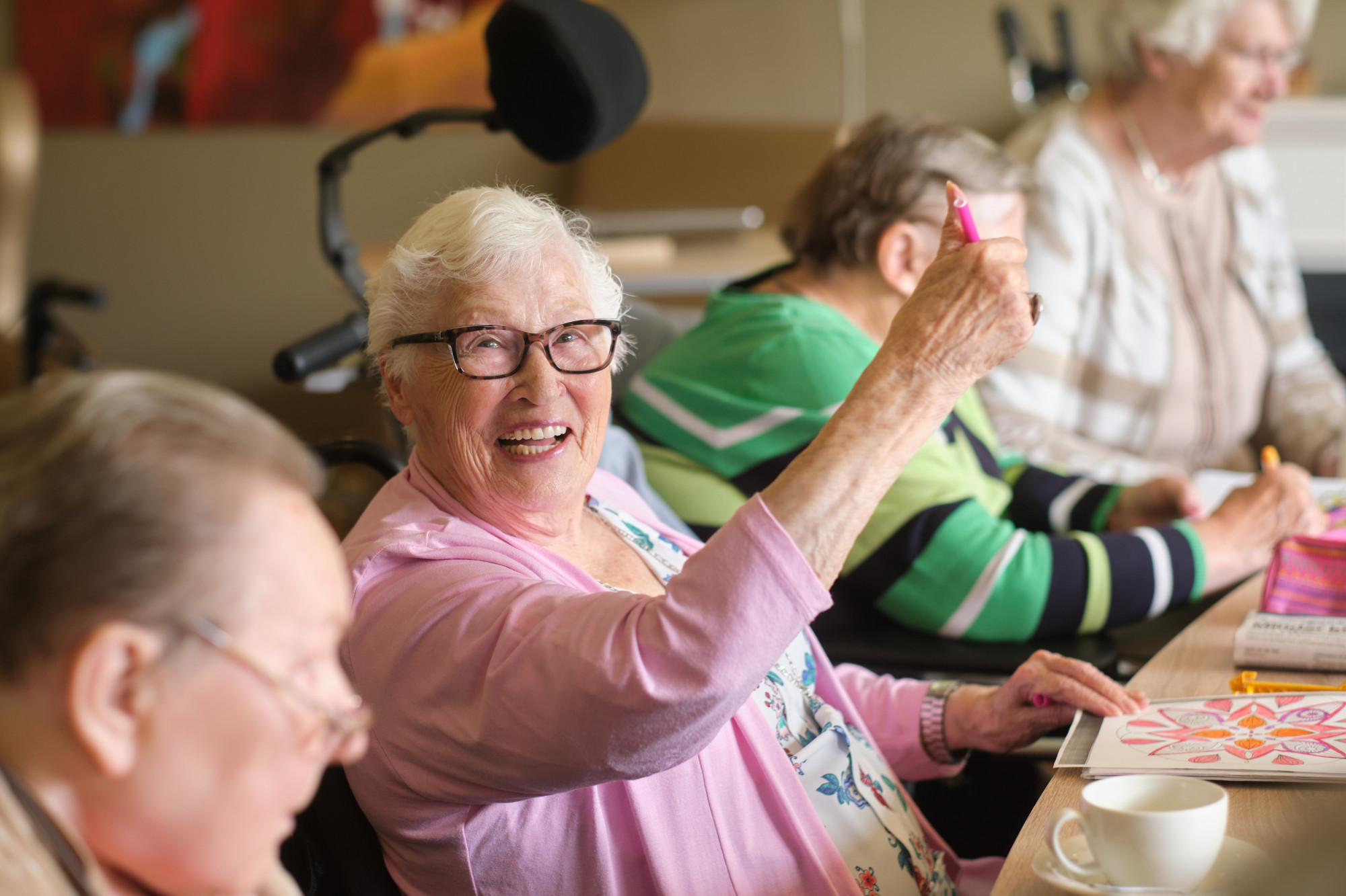 Een groep cliënten en verzorgenden zitten aan tafel koffie te drinken